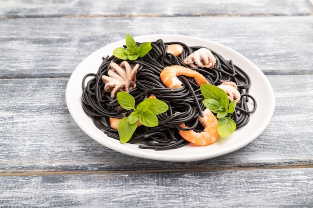 Macarrão de tinta de choco preto com camarões ou camarões e pequenos polvos em superfície de madeira cinza