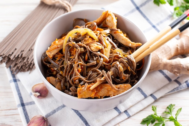 Macarrão de trigo sarraceno com legumes e carne decorado com gergelim em uma tigela sobre uma mesa