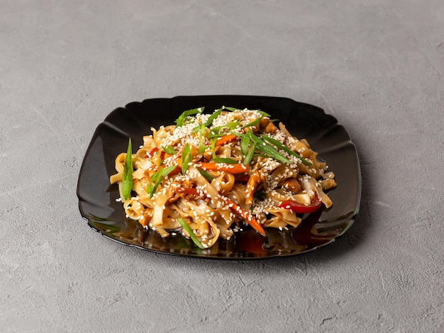 Macarrão de udon de comida vegetariana asiática com cogumelos gergelim e pimenta closeup em uma placa preta