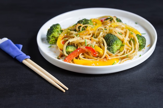 Macarrão de udon frite japonês com legumes na mesa preta, cozido no wok