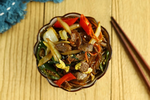 Macarrão de vidro coreano Japchae salteado servido na tigela com fundo de madeira