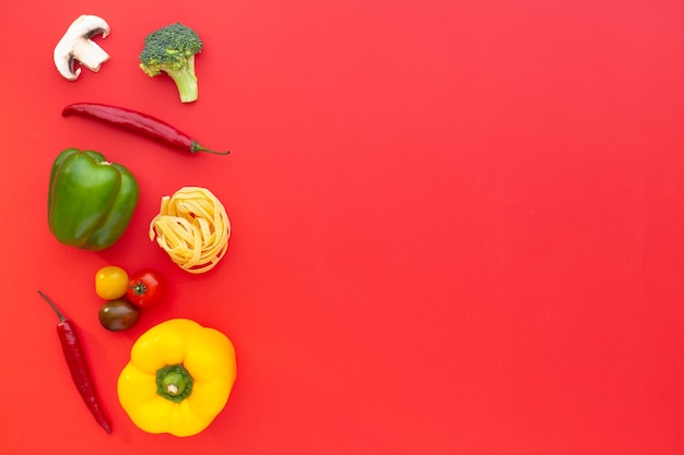 Macarrão e vegetais crus de tagliatelle em fundo vermelho vista superior copie a receita culinária do espaço