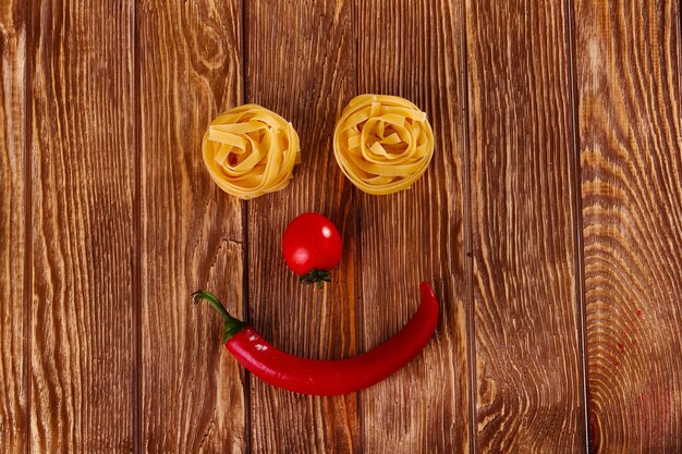 Macarrão em fundo de madeira com vista superior de tomate e pimenta