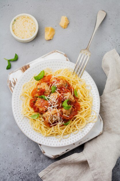 Macarrão espaguete com molho de tomate, queijo parmesão, manjericão e almôndegas em um prato de cerâmica branca na superfície de concreto cinza