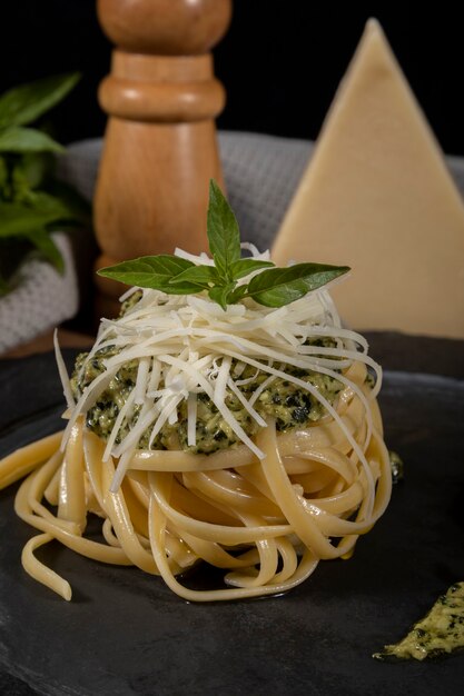 Macarrão espaguete com molho pesto e folhas frescas de manjericão em prato de pedra preta com fundo de madeira.