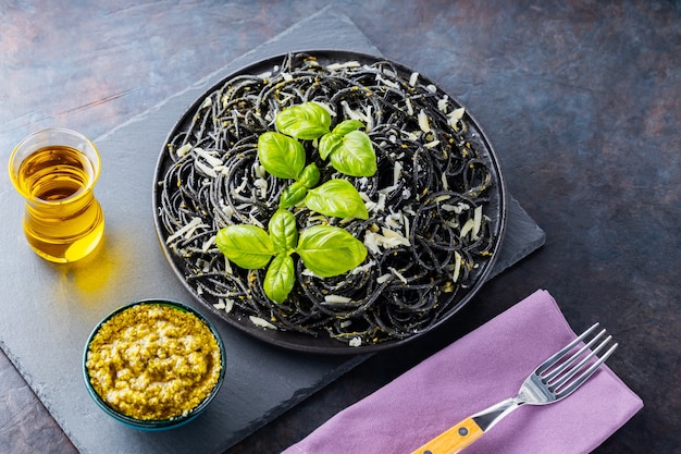 Macarrão espaguete com queijo parmesão, manjericão e molho pesto. Macarrão preto com tinta de choco em um fundo escuro. Massa vegetariana com pesto de manjericão. Vista do topo. Copie o espaço