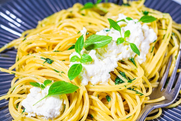 Macarrão espaguete com ricota e manjericão fresco em um prato cinza.