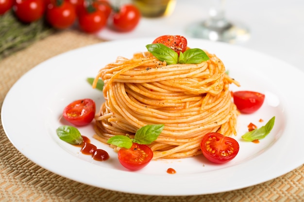 Macarrão espaguete com tomate cereja e folhas de manjericão em prato branco