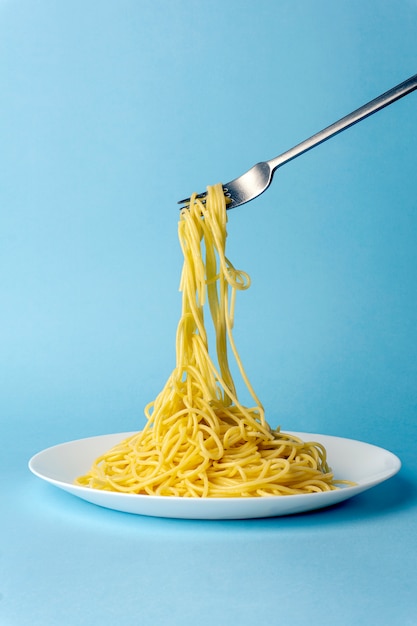 Macarrão espaguete com um garfo em um prato branco sobre um fundo azul