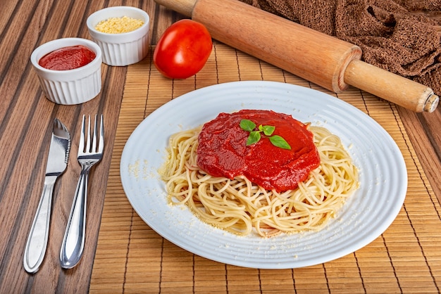 Macarrão espaguete italiano clássico com molho de tomate, queijo parmesão e manjericão no prato sobre a mesa de madeira.