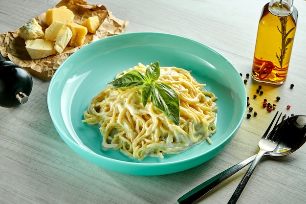 Macarrão espaguete italiano com 4 tipos de queijo em molho de queijo, servido em prato azul sobre mesa de madeira. Comida do restaurante.