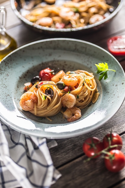 Macarrão espaguete no prato e panela com camarão, molho de tomate, ervas e ervas. cozinha italiana ou mediterrânea.