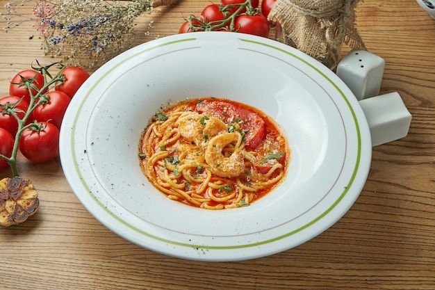 Macarrão espaguete tom inhame com camarão, queijo parmesão e molho vermelho, servido em um prato branco sobre uma mesa de madeira. Cozinha italiana