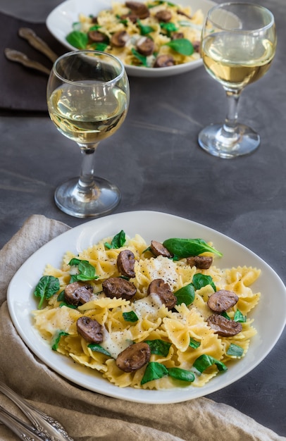 Macarrão farfalle caseiro fresco com cogumelos e espinafre na superfície do concreto.