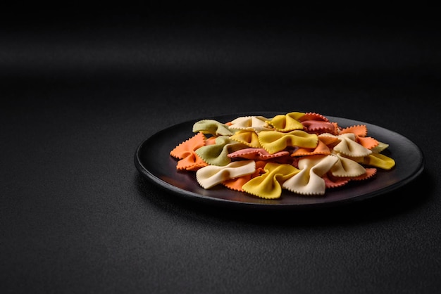 Macarrão farfalle cru em cores diferentes em um fundo escuro de concreto