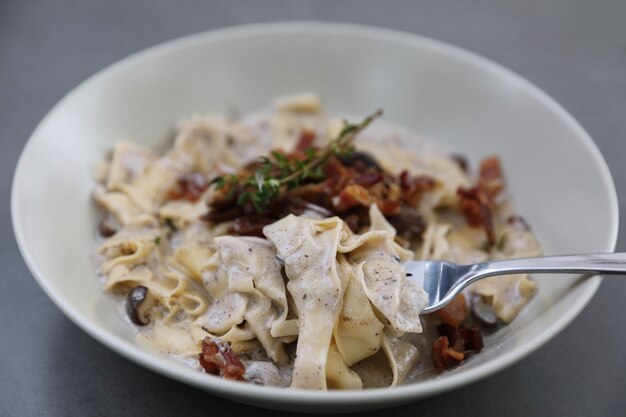 Macarrão fettuccine ao molho alfredo branco com presunto, bacon e cogumelos