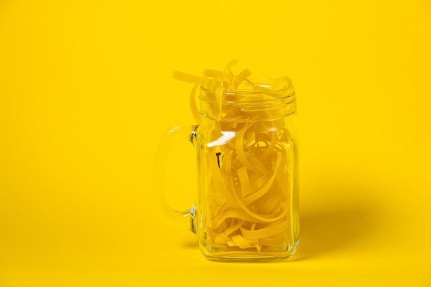 Macarrão fettuccine cru em um copo isolado em fundo amarelo