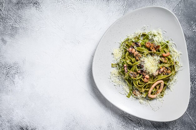 Macarrão fettuccine de espinafre verde com queijo e frutos do mar, camarão, lula, polvo, mexilhão. plano de fundo cinza. vista do topo. copie o espaço.