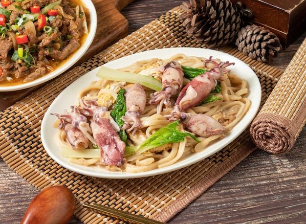 Macarrão frito com rolinhos de ovo estalado em um prato isolado na vista lateral da esteira na mesa de madeira escura comida de taiwan