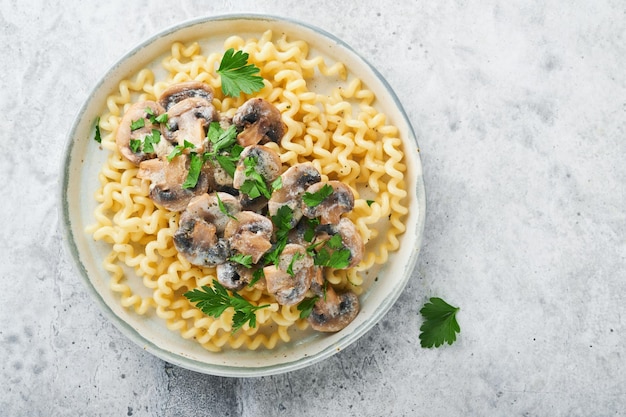 Macarrão Fusilli com cogumelos queijo e molho cremoso de alho no prato na pedra cinza ou fundo de mesa de concreto Vista superior Cozinha tradicional italiana