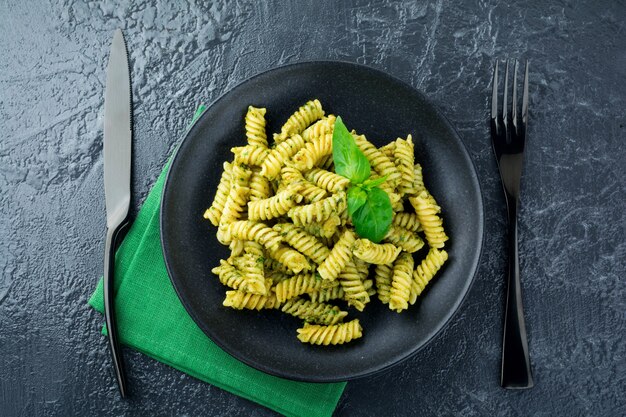 Macarrão Fusilli com molho de manjericão verde abacate e ingredientes na mesa preta. Vista do topo. Copie o espaço.