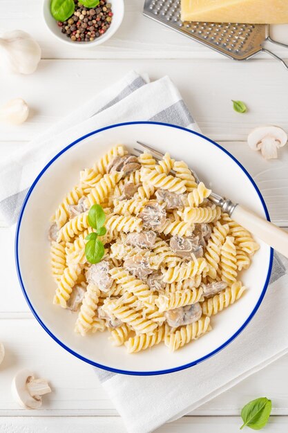 Macarrão Fusilli com queijo de cogumelos e manjericão fresco em um prato sobre fundo branco de madeira