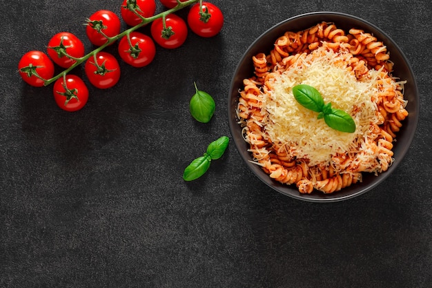 Macarrão fusilli cozido com molho de tomate e parmesão ralado e ramo de tomate cereja no espaço de vista superior de fundo escuro para copiar texto