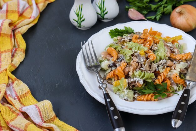 Macarrão Fusilli multicolorido com vegetais em um prato branco no escuro, foco seletivo, espaço de cópia