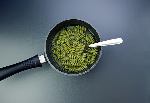 Macarrão fusilli verde em uma colher em um fundo cinza fusilli em uma concha com água