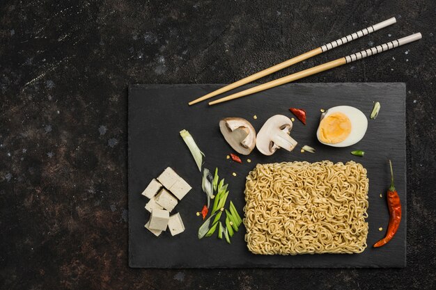 Macarrão instantâneo chinês com cogumelos, ovo, queijo tofu, pauzinhos fundo escuro. Comida asiática.