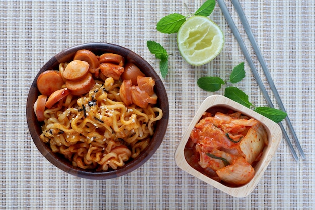 Macarrão instantâneo coreano, picante, salsicha, Kimchi em tigela de madeira com pauzinho no bambo