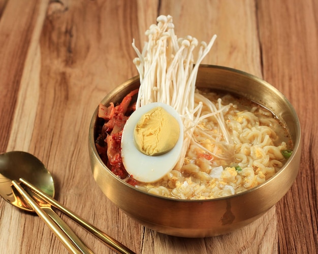 Macarrão instantâneo estilo coreano Ramyeon ou Ramyun com sabor picante coberto com cogumelo meio ovo cozido e Kimchi na mesa de madeira