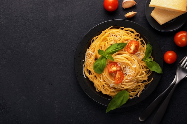 Foto macarrão italiano clássico apetitoso vegetal do espaguete do vegetariano com parmesão da manjericão, do tomate e do queijo na placa preta na tabela escura. ver os de cima, horizontal.