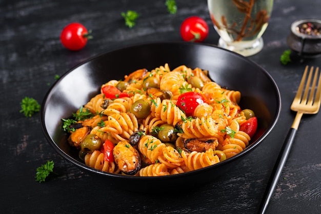 Macarrão italiano clássico fusilli marinara com mexilhões azeitonas verdes e alcaparras na mesa escura Macarrão Fusilli com molho marinara