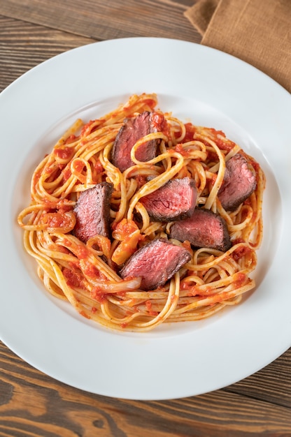 Macarrão linguine com bife fatiado e molho de tomate