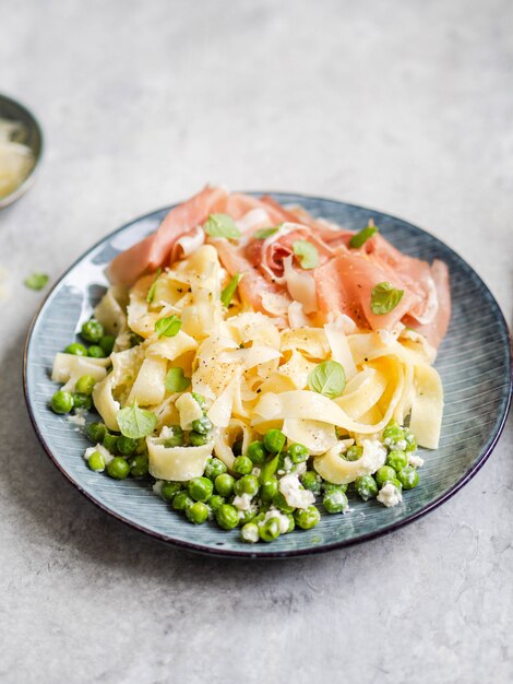 Macarrão linguine com molho branco, ervilhas, parmesão, presunto e hortelã fresca em um prato azul na cinza