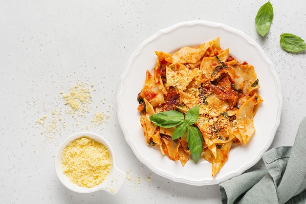 Macarrão Maltagliati com clássico molho de tomate, parmesão e manjericão em mesa de concreto rústica