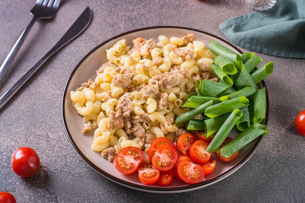 Macarrão naval com tomate cereja e cebolinha em um prato sobre a mesa