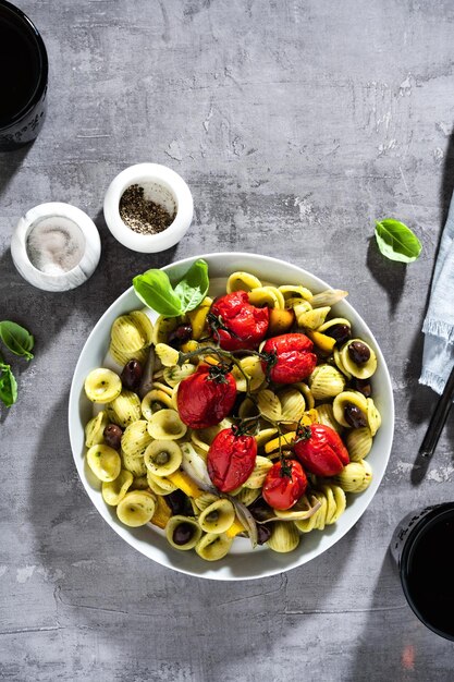 Macarrão Orecchiette com pesto e tomate cereja assado no fundo de pedra com vinho tinto nos copos