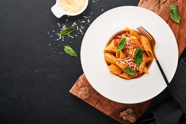 Macarrão penne à bolonhesa Macarrão penne italiano clássico apetitoso saboroso com manjericão parmesão e molho à bolonhesa em chapa branca no prato fundo escuro preto Cozinha italiana tradicional Vista superior