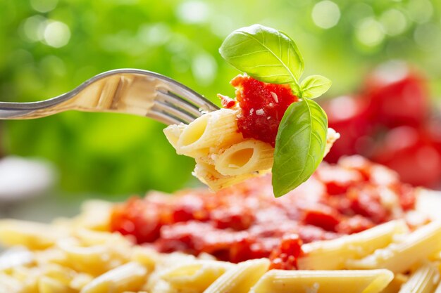 Macarrão penne com molho de tomate e manjericão verde em um garfo