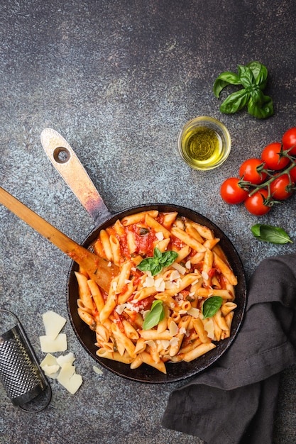 Macarrão penne com molho de tomate e queijo decorado com manjericão em pedra cinza