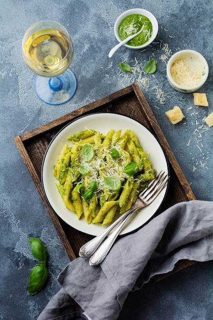 Macarrão penne com queijo parmesão e folhas de manjericão em placa de cerâmica na mesa de concreto velha vintage cinza.