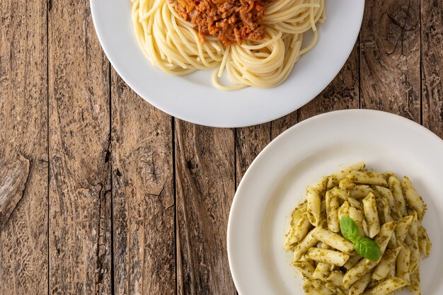 Macarrão penne e espaguete com pratos de molho à bolonhesa em mesa de madeira