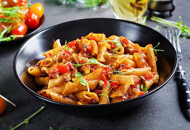 Macarrão penne em molho de tomate com carne, tomate decorado com brotos de ervilha sobre uma mesa escura