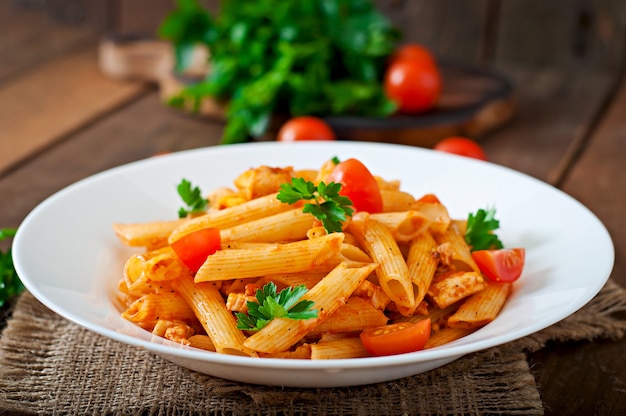 Macarrão penne em molho de tomate com frango e tomate em uma mesa de madeira