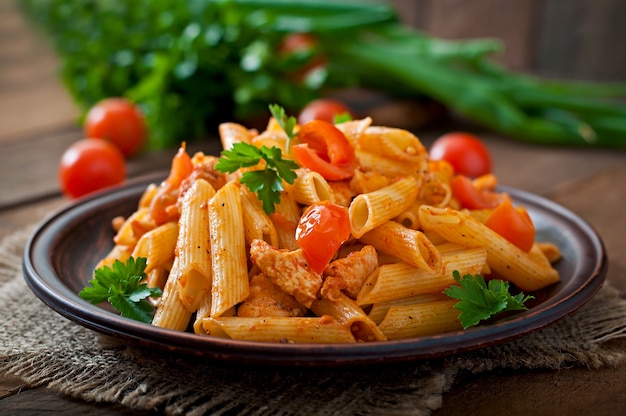 Macarrão penne em molho de tomate com frango e tomate em uma mesa de madeira