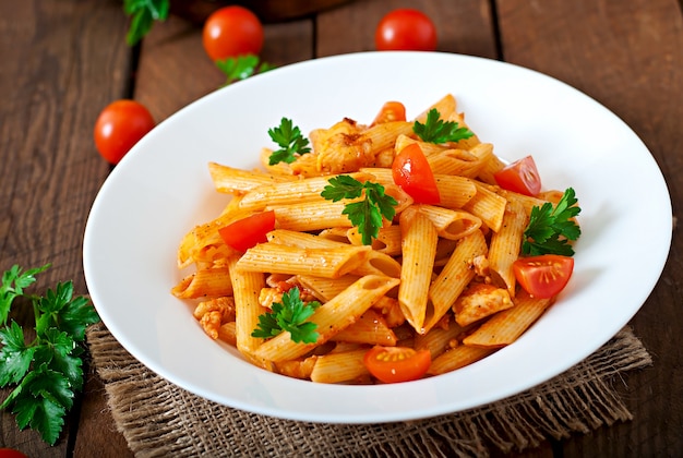Macarrão penne em molho de tomate com frango e tomate em uma mesa de madeira
