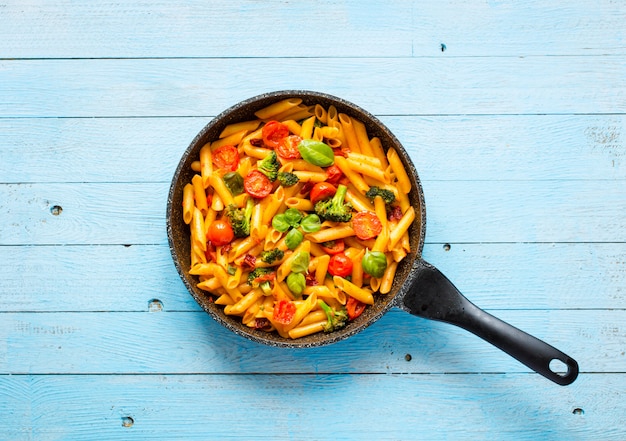 Macarrão penne italiano em molho de tomate e diferentes tipos de legumes, em uma mesa de madeira