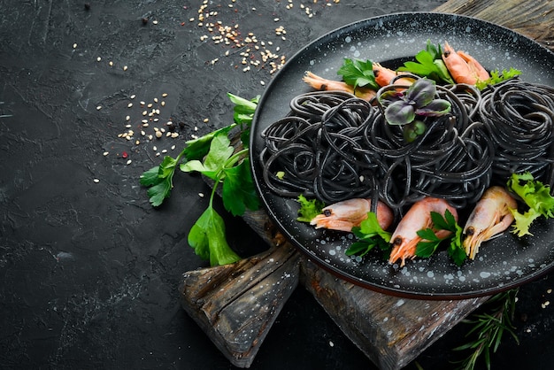 Macarrão preto com camarões em um prato preto Vista superior Em um fundo preto Espaço para cópia gratuita